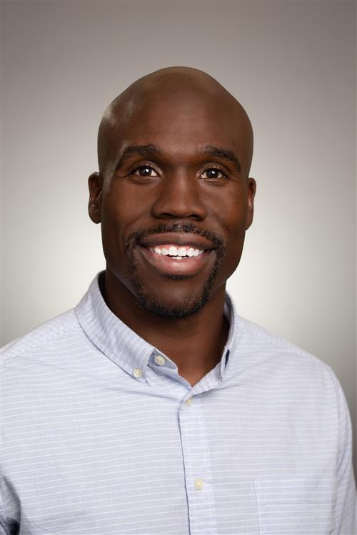A man with no hair smiling in a blue-purple shirt